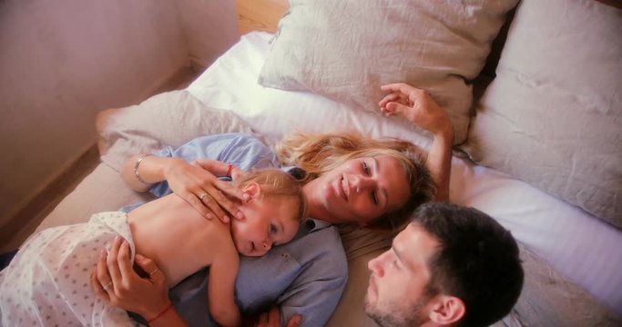 Loving parents relaxing in bed with little baby son