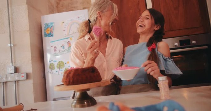 Grandmother and granddaughter having fun icing homemade cake in kitchen