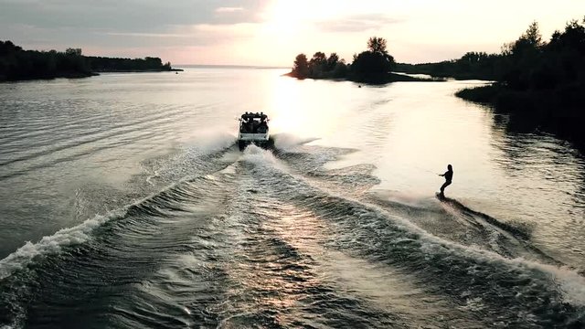 Copter follow behind wakeboarder surfing. Aerial view of wakeboarding on river in sunshine.