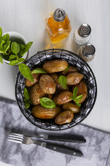 Baked potatoes in a black basket. Knife and fork. Olive oil, salt, pepper, basil. The background is white. Copy space. Top view. Vertical shot.