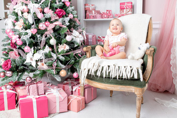 Cute little baby in vintage chair and christmas gifts. Little child having fun near Christmas tree in living room. Loving family Merry Christmas and Happy New Year. © malkovkosta