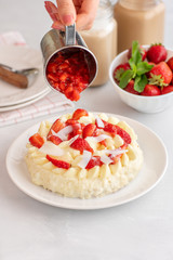 women's hands pour the sauce on the cake. Delicate strawberry cheesecake with coconut. Delicious homemade cake with Fresh berries on light table.