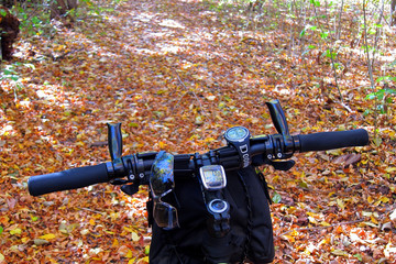 Bicycle handlebar with a speedometer and a clock against the background of a forest road covered...