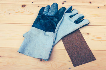 leather work gloves and sandpaper on wooden plank