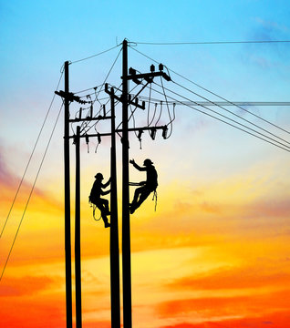 Silhouette Electrical engineers working on electricity pylon high tension power line repairs and maintenance  on blurry sunset background