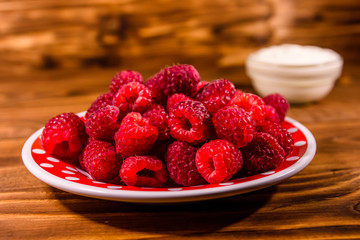Ceramic plate with ripe raspberries and sour cream on wooden table