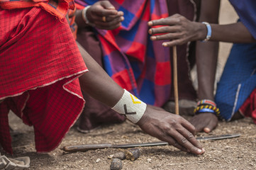 Fototapeta premium Traditional tribal bead work worn around wrist by Masai man as he lights a fire using traditional method of stone and stick. Tanangire National Park, Tanzania