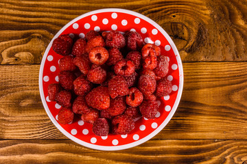 Ceramic plate with ripe raspberries on wooden table. Top view