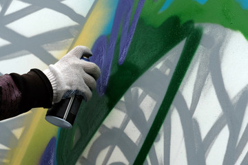 The artist's hand with a paint balloon draws graffiti on a white wall.
