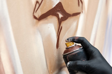 A street artist in black gloves draws an abstract image using a brown spray paint. Graffiti concept. Close-up of a hand with a ballon. © romsvetnik