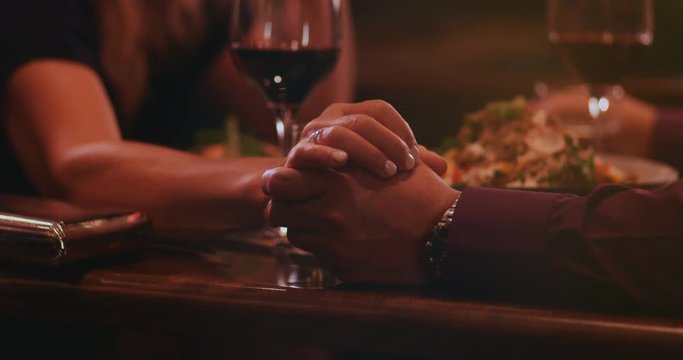 Close-up of mature couple holding hands on dinner date night