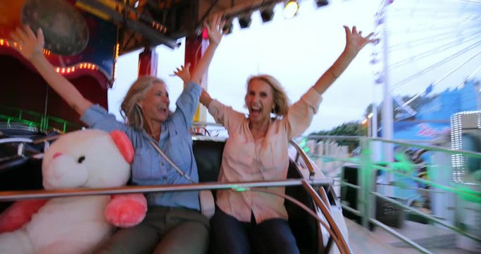 Excited mature women enjoying roller coaster ride with arms outstretched