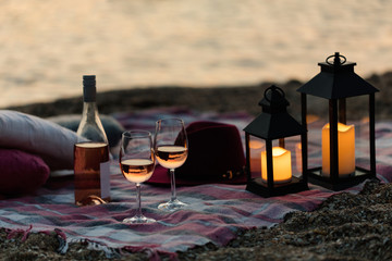 Summer sea sunset. Romantic picnic on the beach. Bottle of wine, glasses, candles, plaid and pillows.