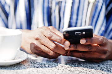 Close up hands of african man with mobile phone and cup of coffee.
