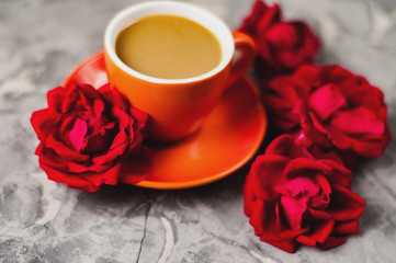 Full cup of coffee with milk beside red roses on old gray concrete surface. Love concept