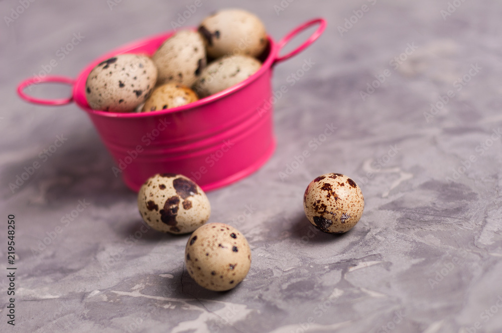 Wall mural One pink metal rural basin with handles full of spotted fresh quail eggs beside three scattered eggs on old broken worn gray cement floor