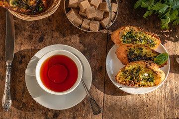 Lunch - tea and traditional French baguette toast with butter, parsley, garlic and basil on an old rustic wooden table