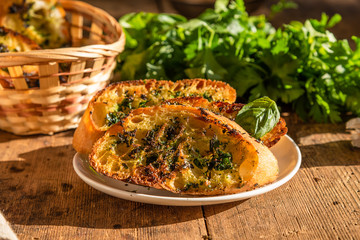 French baguette toast with butter, parsley, garlic and basil on an old, rustic wooden table