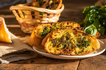 French baguette toast with butter, parsley, garlic and basil on an old, rustic wooden table