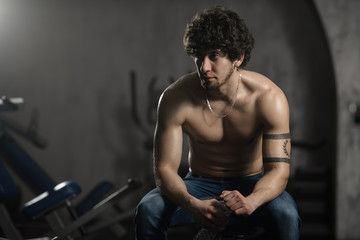 Fototapeta na wymiar Young attractive man resting in gym after exercising, male posing