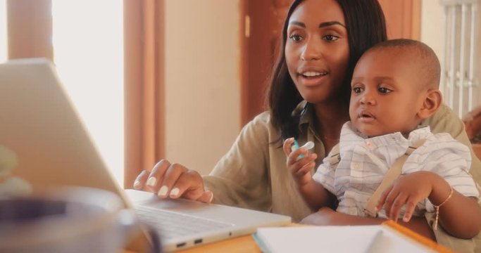 Mother with baby son using laptop and working from home