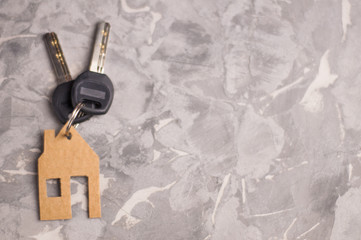 Two shiny metal keys with black plastic handle tied to handmade house of brown goffred cardboard on old gray dirty cement floor with copy space. Estate concept