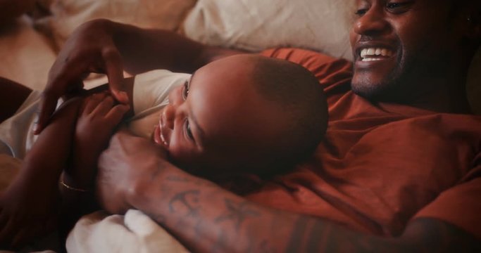 Happy loving father playing with little son in bed