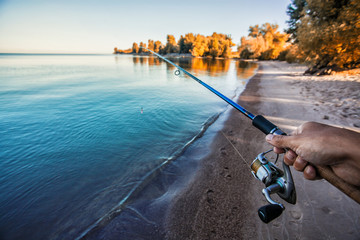 hand with spinning and reel on the summer lake