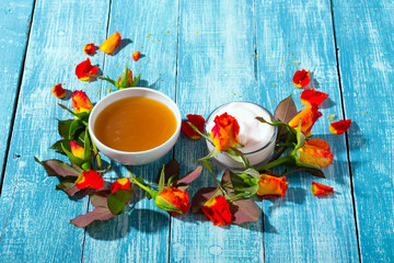 cosmetic creams and rose flowers on blue wooden table background