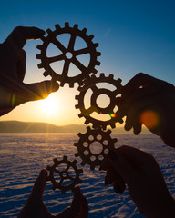 gears in the hands of a group of people against the setting sun. concept teamwork.