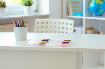 Interior of child room with white table and colorful pencils on him and shelf with books