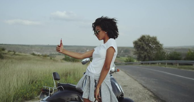 African girl with curly Afro hair takes selfies in the beautiful nature, loving that vibe.