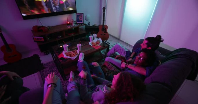 Young multi-ethnic roommates relaxing on sofa and watching TV together