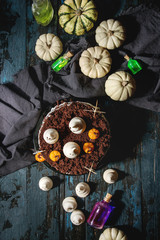 Halloween sweet table with cemetery chocolate cake, marzipan and decorative pumpkins, meringue ghosts, poison's bottles over black wooden background. Flat lay, space