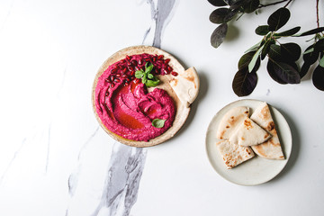 Homemade spread beetroot hummus with pomegranate seeds, olive oil, basil served on ceramic plate...
