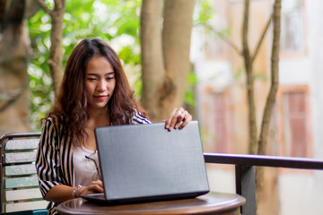 Young freelance woman using laptop to work outside coffee shop. Business person using laptop to communicate. Female student using laptop and study outside cafe in free time.