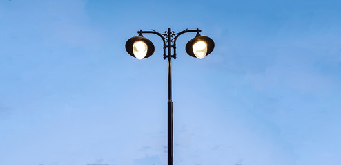 modern street lamp shines against a background of blue sky at sunset