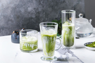Matcha green tea iced latte or cocktail in three different glasses with ice cubes, matcha powder...