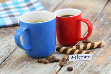 Welcome card with two colorful mugs of coffee on wooden surface
