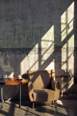 soft armchair and table in a large sunny room with a shadow on the wall