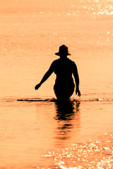 Fototapeta na wymiar silhouette of woman with hat in the sea at sunset