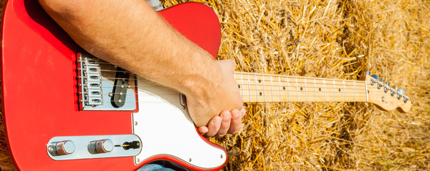 Guitar telecaster in red with a wooden stamp in the hand of a musician background of straw on a sunny summer day
