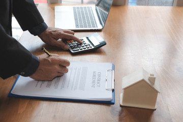 businessman using calculator to calculate invoice with house model. mortgage, real estate, property concept