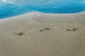 traces of human feet on black sand near the water on the beach. Background texture.