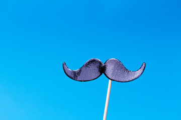 Fake mustache on the stick on blue background - symbol of Movember, event to raise awareness...