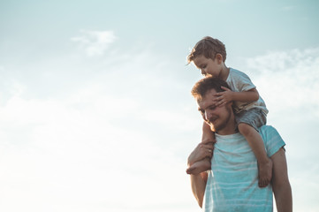 Happy kid playing with father. Dad and son outdoors. Father carrying child on his back. Happy family in summer field