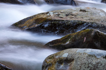 Water rushing around three large rocks in a cold mountain stream, horizontal aspect