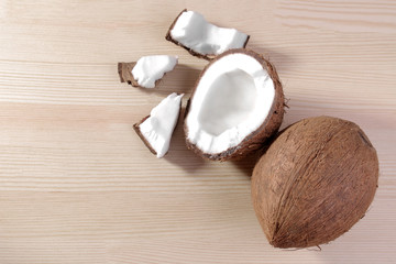 a large fresh coconut and pieces of coconut on a natural wooden background. top view