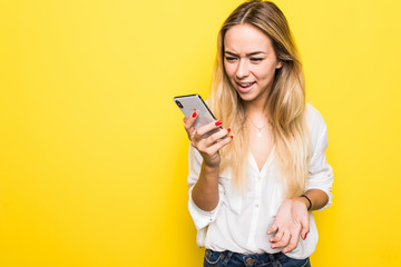 Displeased young woman standing isolated over yellow background using mobile phone.