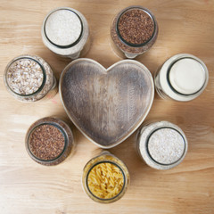 Various uncooked cereals, grains, and pasta for healthy cooking in glass jars on wooden table. Top view. Clean eating, balanced dieting food. Square image.